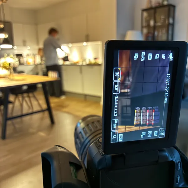 En kameraskærm med WeHerb-pakker på en hylde under optagelsen af kampagnevideoen